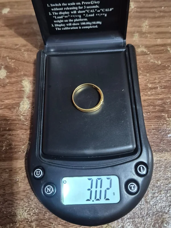 Satu cincin emas polos di timbangan digital menunjukkan 3,02 gram