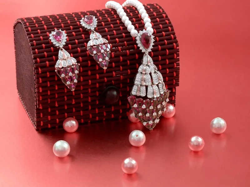 Sepasang anting dan liontin bertatahkan batu merah dan berlian, dengan untaian mutiara di atas kotak perhiasan anyaman